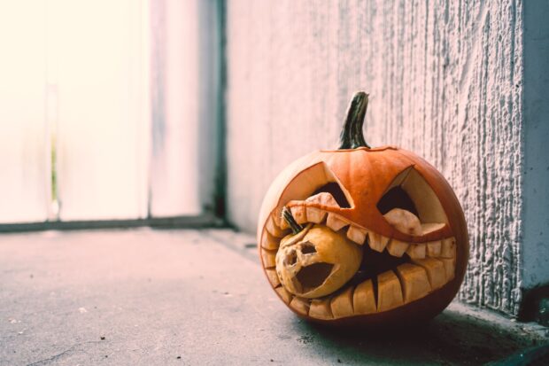 A Halloween pumpkins scene shows a large pumpkin carved with sharp teeth holding a smaller pumpkin inside its mouth, HD Desktop Wallpaper