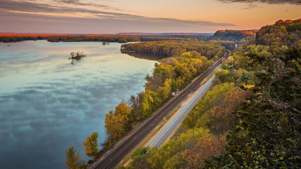 A peaceful view of the Mississippi River flowing beside colorful autumn trees at sunset, HD Desktop Wallpaper