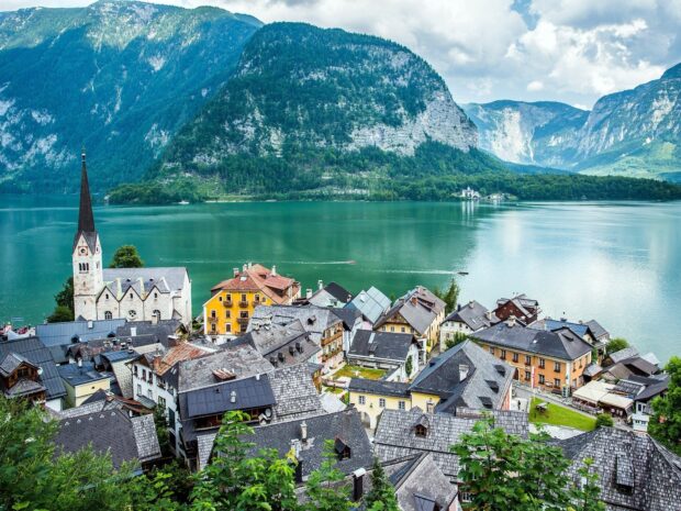 A scenic village sits peacefully by a tranquil lake surrounded by towering mountains in Austria, HD Desktop Wallpaper