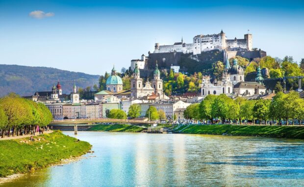 A scenic view of Austria with historic buildings along the river under a clear sky, HD Desktop Wallpaper