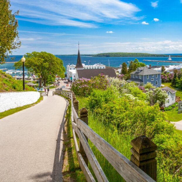 A sunny pathway leads to Mackinac Island with houses, trees, and a lake in the background, HD Desktop Wallpaper