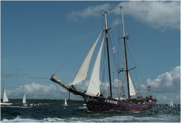 A classic schooner sailing on the ocean with white sails against a cloudy sky
