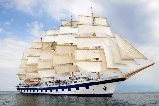 A majestic schooner sailing on calm waters under a clear sky with fully unfurled sails
