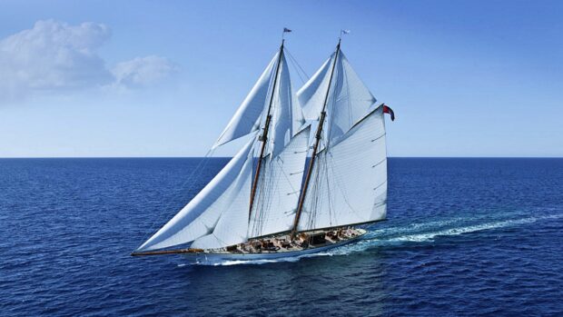 A schooner sailing smoothly across the deep blue ocean under a clear sky