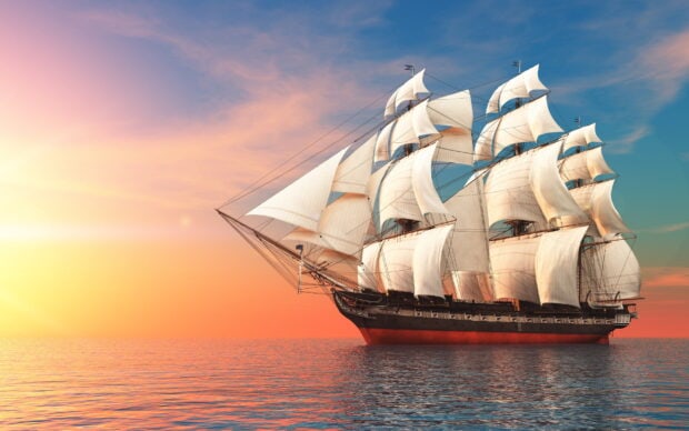 Classic schooner sailing on calm ocean during vibrant sunset