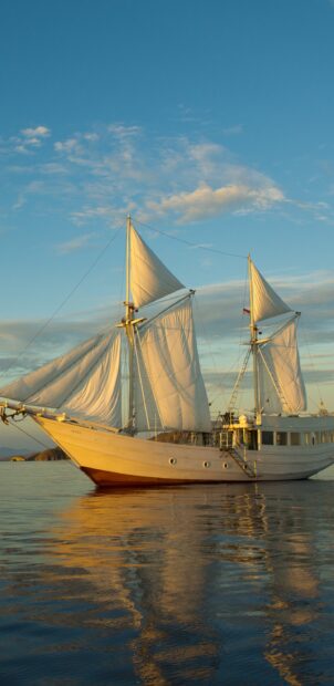 A schooner sailing calmly on reflective water during golden hour