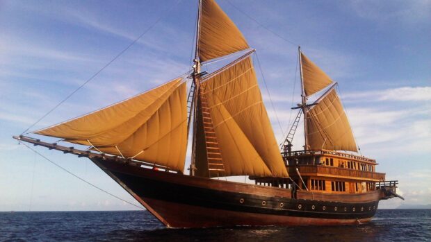 A traditional schooner sailing on calm ocean waters with large tan sails