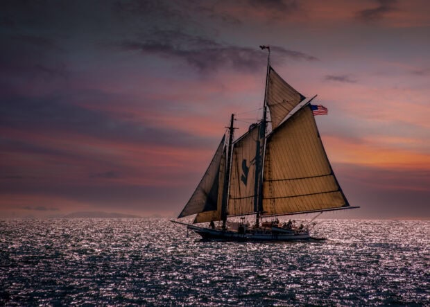 A schooner sailing on shimmering ocean waters during a colorful sunset
