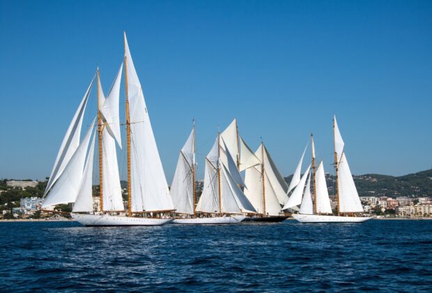 Multiple schooner sailing vessels with white sails on a calm blue sea