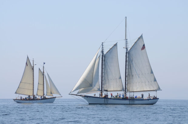 Two schooners sailing on calm sea with people on board under clear sky