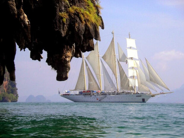White schooner sailing near rocky cliffs on clear calm water
