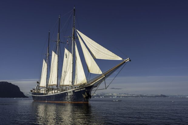 A classic schooner sailing on calm waters under clear blue sky
