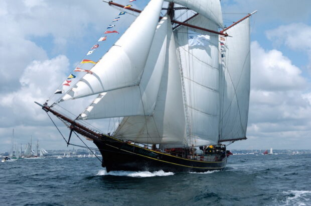 A classic schooner sailing on the ocean with full white sails under a cloudy sky