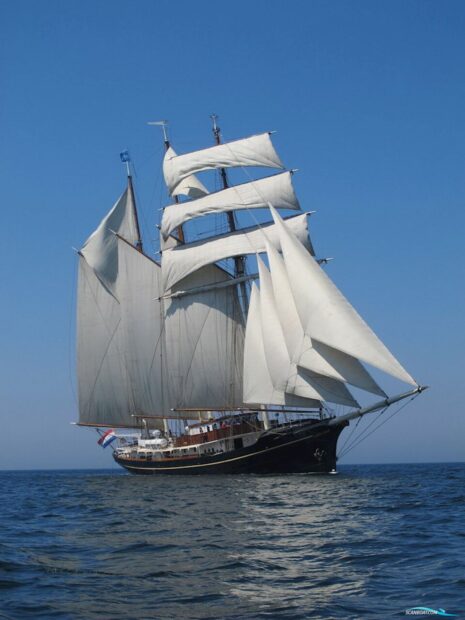 A classic schooner with white sails sailing on calm blue sea under clear sky