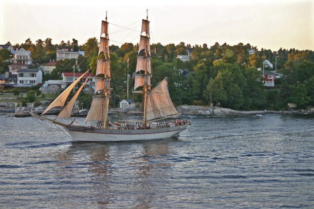 A classic schooner sailing near a coastal town with lush green trees