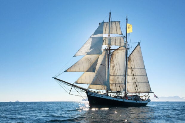 A schooner sailing on calm blue ocean under clear sky with full white sails