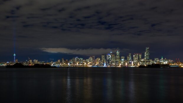 The Seattle skyline shines brightly at night with city lights reflecting on the water, 4K Desktop Wallpaper