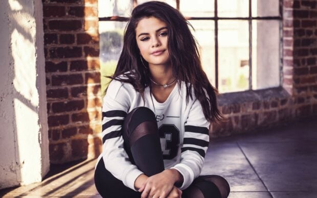 Selena Gomez is sitting on the floor wearing a white sweatshirt and black leggings, 2K Desktop Wallpaper
