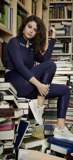 Selena Gomez is sitting surrounded by stacks of books wearing a navy outfit, HD Mobile Wallpaper
