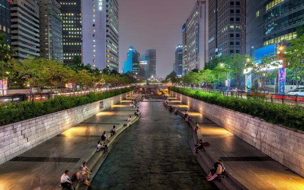 People relaxing by the urban stream in Seoul Korea cityscape at night with modern buildings