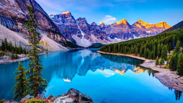 A peaceful mountain lake reflects the surrounding rocky peaks and green trees under a clear sky, 4K Desktop Wallpaper
