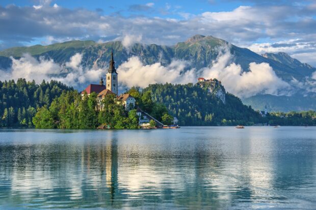 A mountain lake with a church on the island surrounded by calm water and misty mountains, 2K Desktop Wallpaper