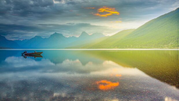 A calm lake reflects mountains under a cloudy sky in Glacier National Park, 4K Desktop Wallpaper