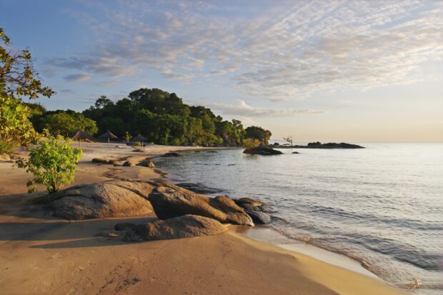 A peaceful shore with rocks and lush trees captures the beauty of Malawi landscapes, 2K Desktop Wallpaper