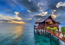 A tropical bungalow sits peacefully over clear blue water under a dramatic sunset sky, HD Desktop Wallpaper
