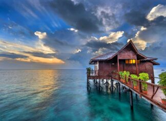 A tropical bungalow sits peacefully over clear blue water under a dramatic sunset sky, HD Desktop Wallpaper