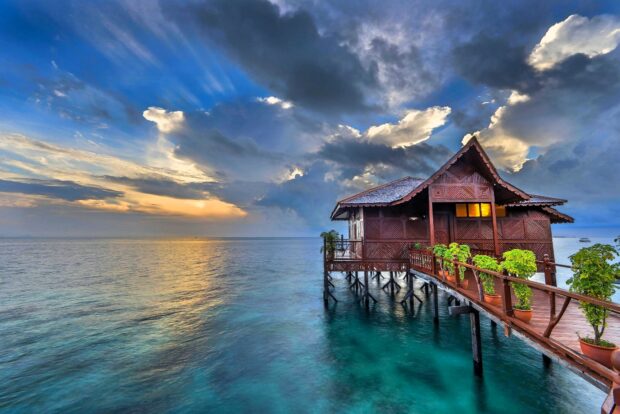 A tropical bungalow sits peacefully over clear blue water under a dramatic sunset sky, HD Desktop Wallpaper