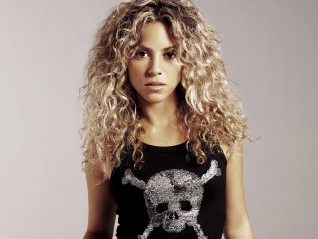 Shakira wallpapers features a woman with curly blonde hair wearing a black shirt with a skull design, HD Desktop Wallpaper
