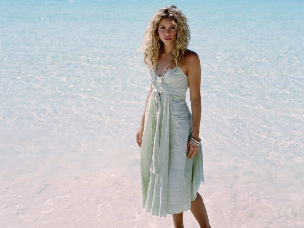 Shakira standing in clear ocean water wearing a light dress with bracelets on her wrist, HD Desktop Wallpaper