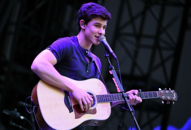 Shawn Mendes playing guitar and singing on stage during a live performance