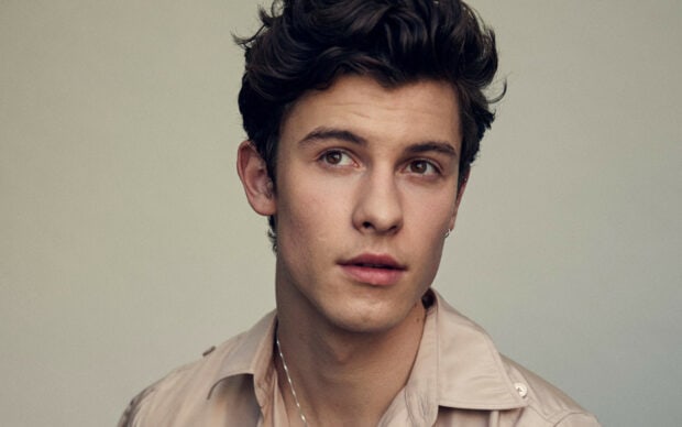 Young man with curly hair looking away wearing a beige shirt with a silver necklace