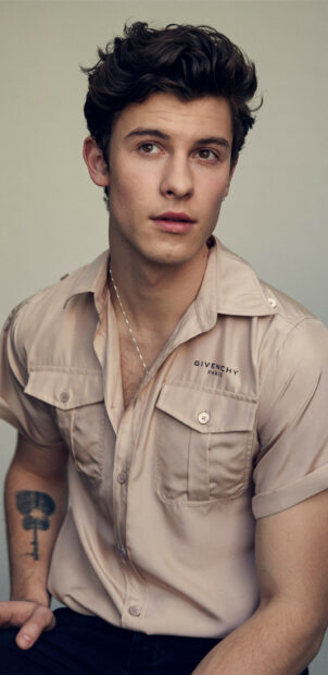 Shawn Mendes wearing a beige Givenchy shirt looking thoughtfully to the side