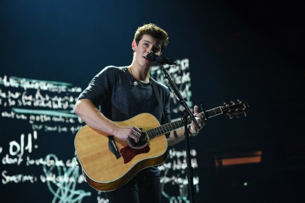 Shawn Mendes playing guitar and singing on stage during a live concert