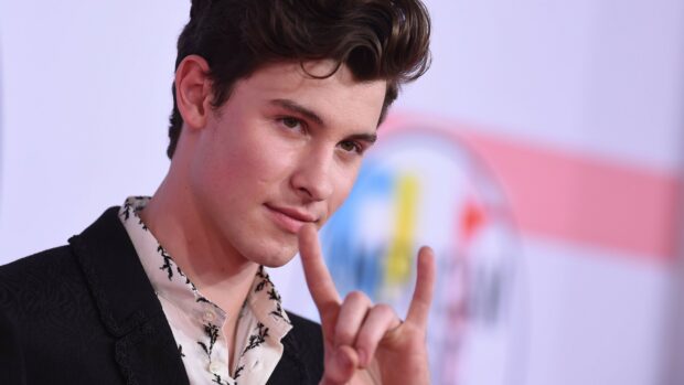 Shawn Mendes posing with hand gesture and wearing a patterned shirt and black jacket
