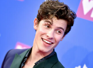 Shawn Mendes smiling at an event with curly hair and a green suit jacket