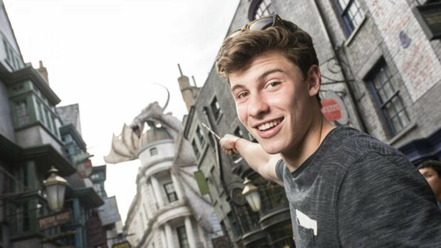 Shawn Mendes pointing at a dragon statue in a city street with a smile