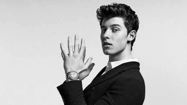 Shawn Mendes showing his wristwatch in a black textured jacket in a monochrome style