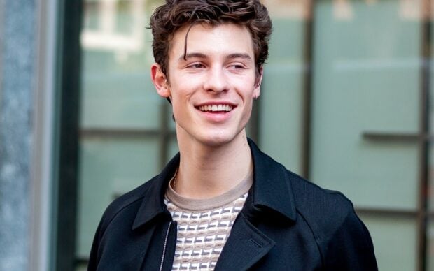 Shawn Mendes smiling outdoors wearing a patterned shirt and black jacket