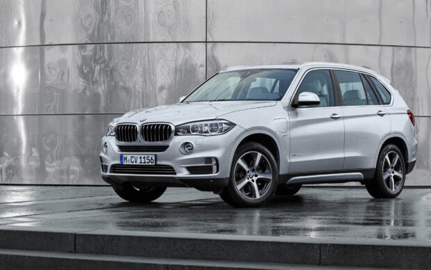 A silver BMW X5 SUV is parked on a wet surface with a modern metallic wall background, 2K Desktop Wallpaper