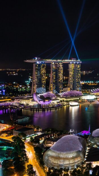 Night view of Singapore skyline with illuminated buildings and light beams over the bay