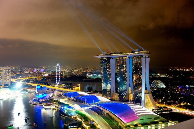 The Singapore skyline features the iconic Marina Bay Sands and vibrant city lights at night