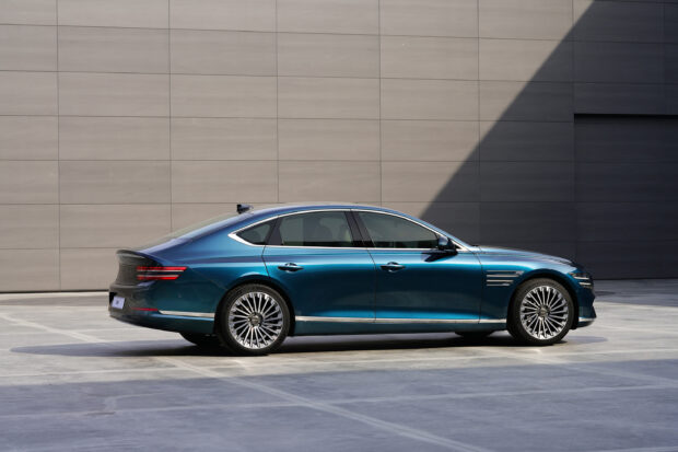 A sleek blue Genesis car is parked beside a modern building in bright sunlight, 2K Desktop Wallpaper