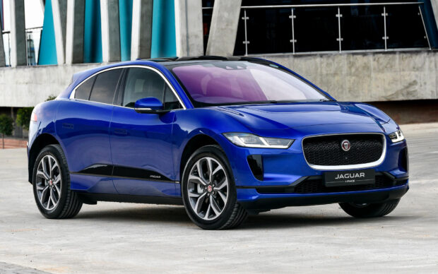 A sleek blue Jaguar I Pace is parked near a modern building showcasing its electric SUV design, HD Desktop Wallpaper