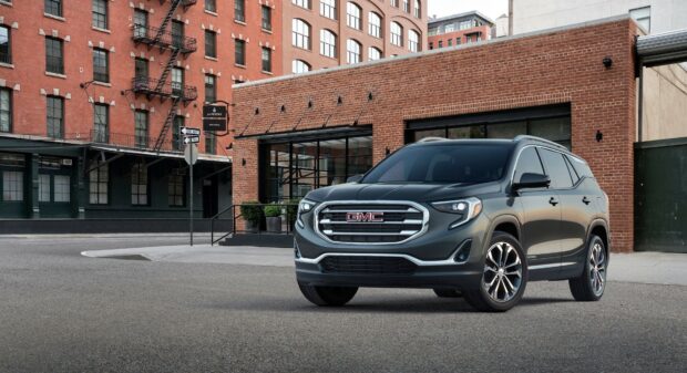A sleek GMC SUV is parked in front of a red brick building in an urban area, 4K Desktop Wallpaper
