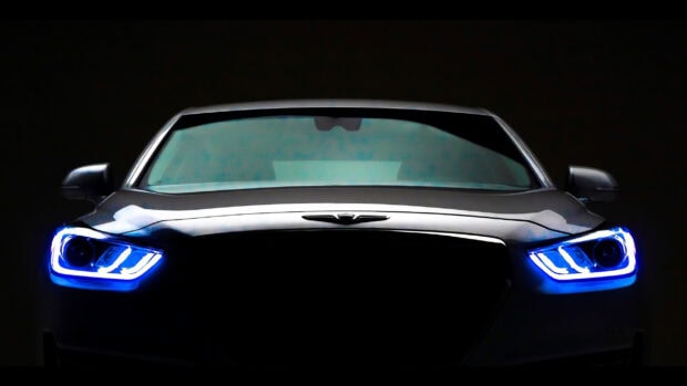 A sleek Genesis car is shown with bright blue glowing headlights in dark surroundings, 2K Desktop Wallpaper