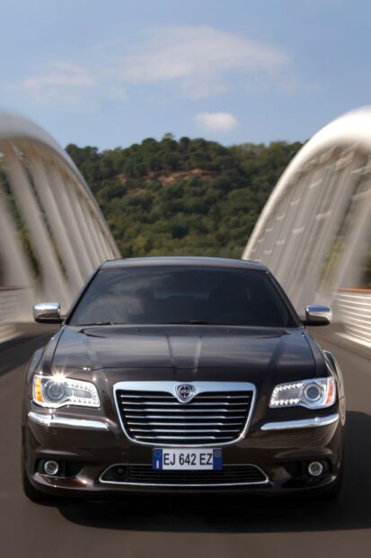 A sleek Lancia car is driving across a modern bridge with trees in the background, HD Mobile Wallpaper